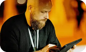 Ein Veranstaltungstechniker konzentriert sich auf ein Tablet während einer Outdoor-Veranstaltung. Der Hintergrund, verschwommen und hell in bernsteinfarbenen Tönen beleuchtet.