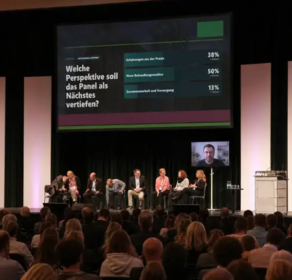 Podiumsdiskussion mit zugeschaltetem Gast und Ergebnissen einer Publikumsabstimmung auf der großen Leinwand